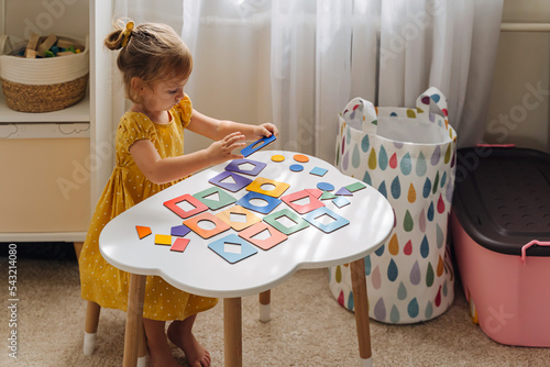 A little girl playing with wooden shape sorter toy on the table in playroom. Educational boards for Color and Shapes sorting for toddler. Learning through play. Developing Montessori activities. photo