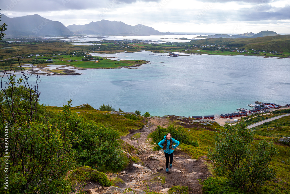 girl with backpack hiking Offersøykammen trail head admiring the panorama of lofoten islands, Norway; hiking in the Norwegian fjords