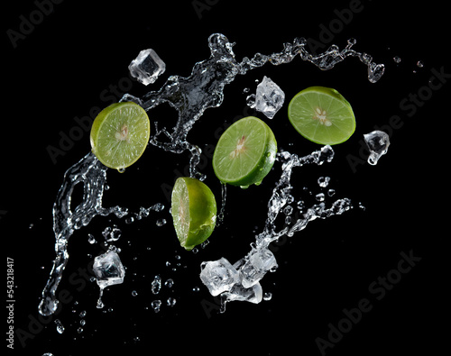 Fresh limes, ice cubes and water splashes, isolated on black background