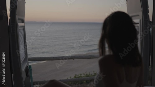 Woman sitting in the back of the camper van motor home watching romantic sunset