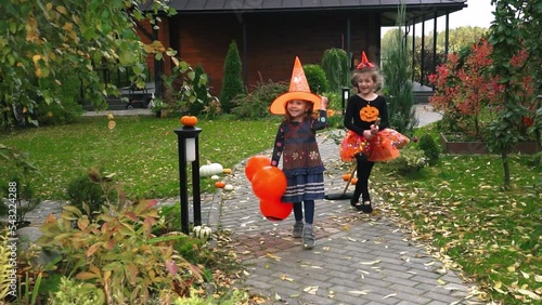 Little girls dressed as witch at Halloween in decorated and hats with orange balls runs path in the garden. . High quality FullHD footage