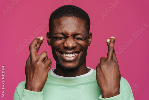 Fototapet Black young man smiling and holding fingers crossed for good luck