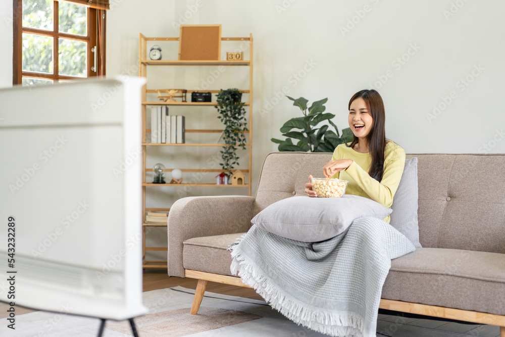 Young asian woman putting a bowl of popcorn on pillow and eating popcorn while sitting on the big comfortable Young asian woman putting a bowl of popcorn on pillow and eating popcorn while sitting on the big comfortable
