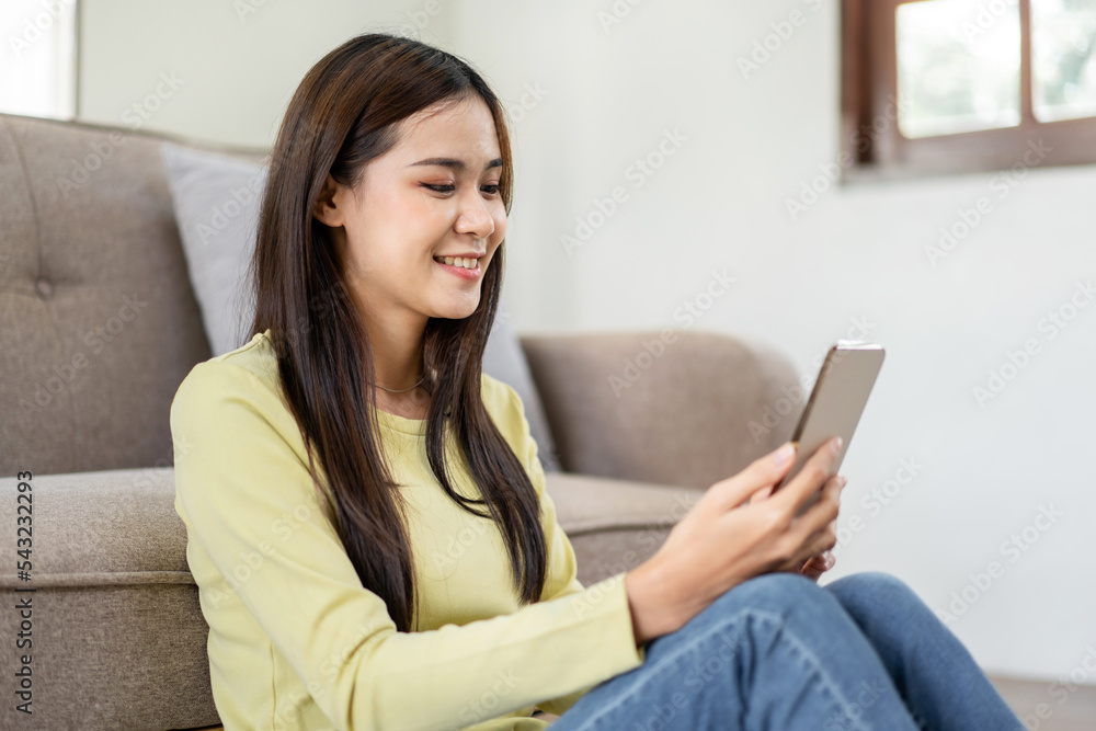 Young woman is sitting on the floor and lean against comfortable sofa and using smartphone to checking Young woman is sitting on the floor and lean against comfortable sofa and using smartphone to checking