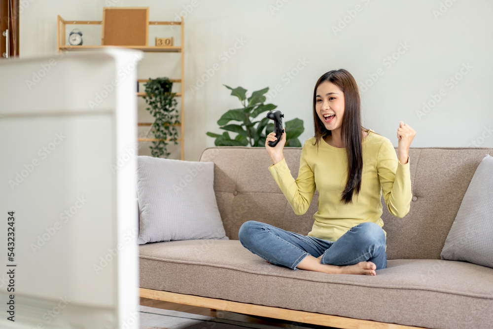 Young asian woman is using video game control joystick to playing games with enjoyment and raising both Young asian woman is using video game control joystick to playing games with enjoyment and raising both