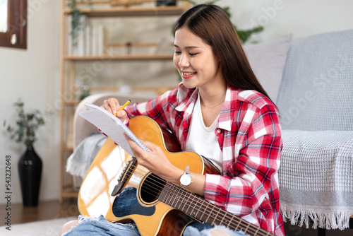 фотографія Young woman is compose song and writing lyrics on notebook while putting guitar