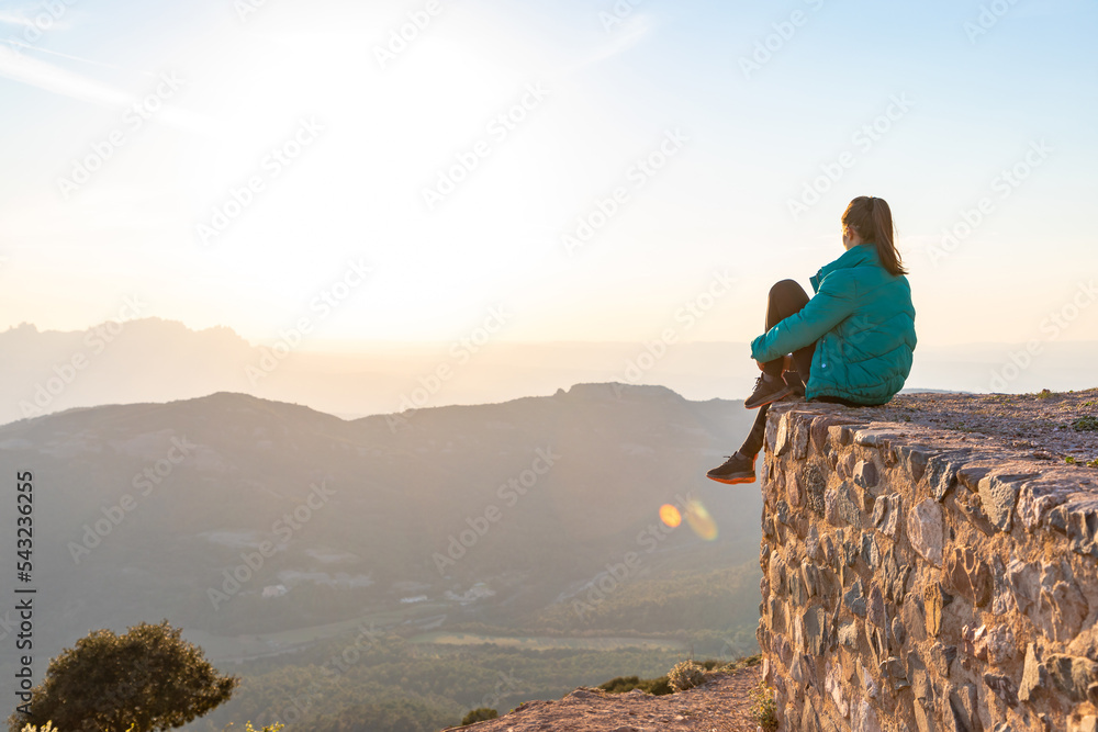 Fototapeta premium Beautiful woman sitting on an edge during sunset with mountains