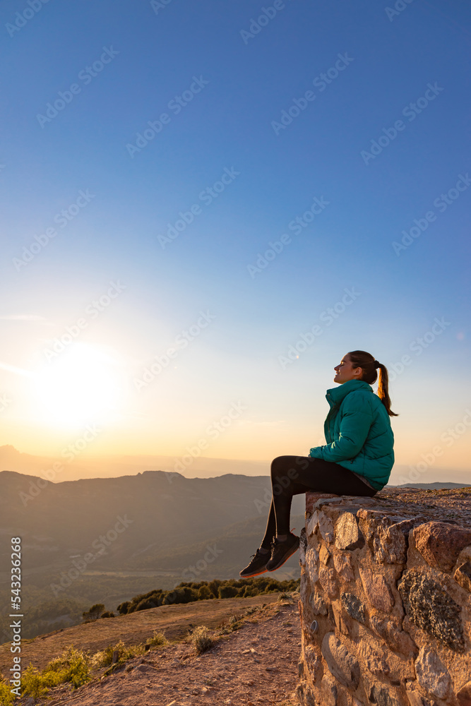 Beautiful woman sitting on an edge during sunset with mountains