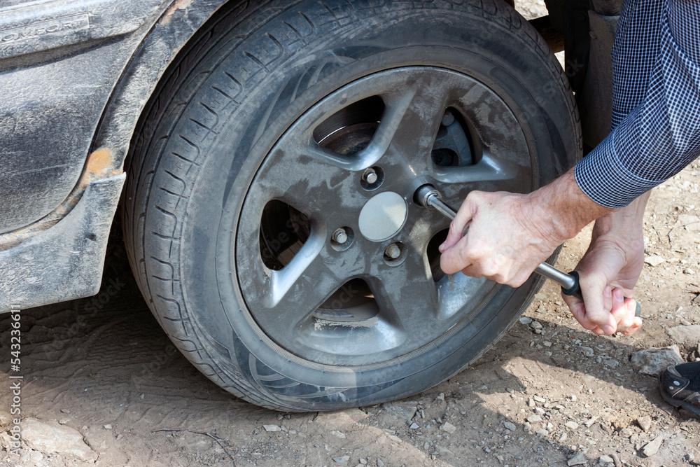 A man unscrews a flat car tire outdoors. Wheel replacement