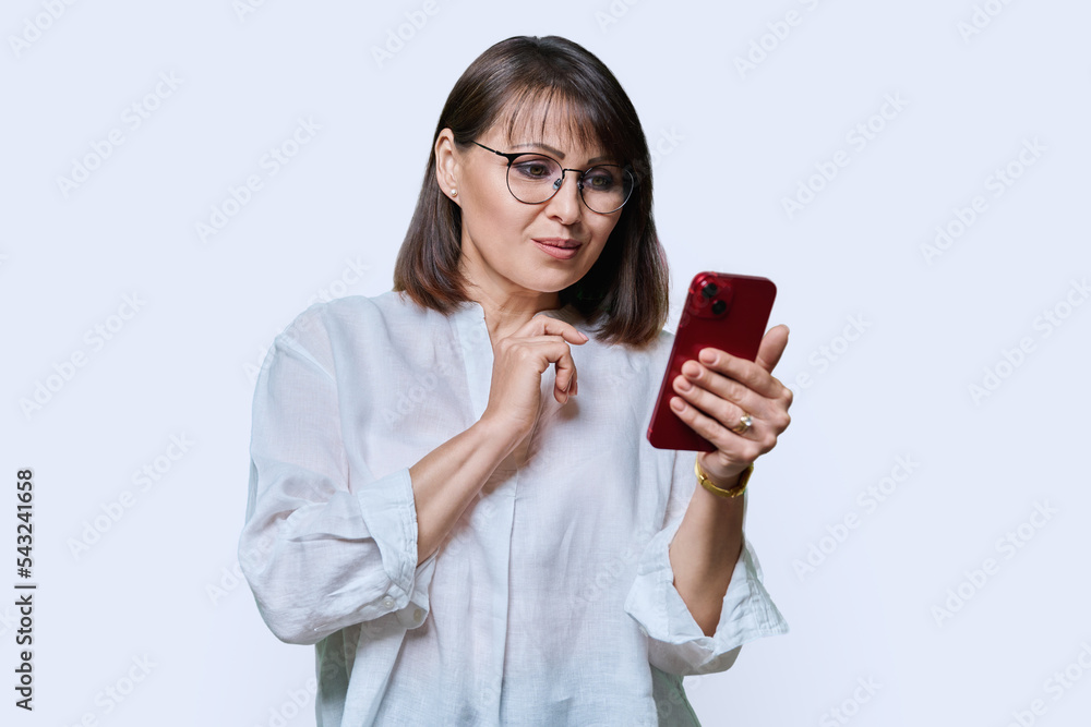 Middle aged focused woman using smartphone on white studio background. Middle aged focused woman using smartphone on white studio background.