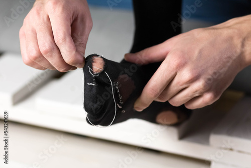 Fotografi A man sews a black torn sock with white threads