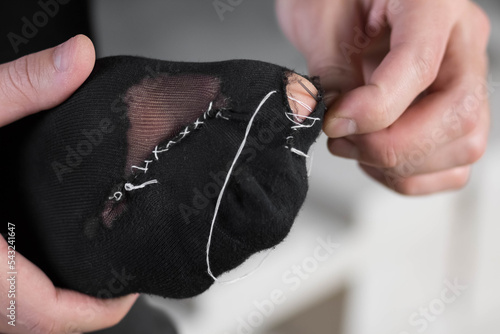 A man sews a black torn sock with white threads. Closeup. Isolated on a white background