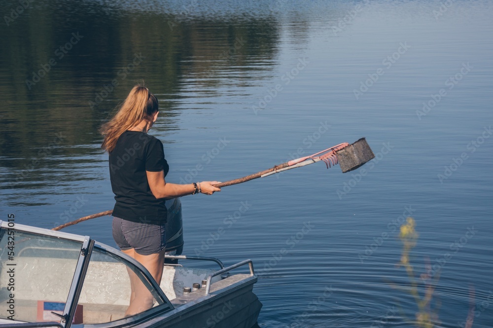 Woman with fishing gaff in motor boat on river on sunny day Woman with fishing gaff in motor boat on river on sunny day