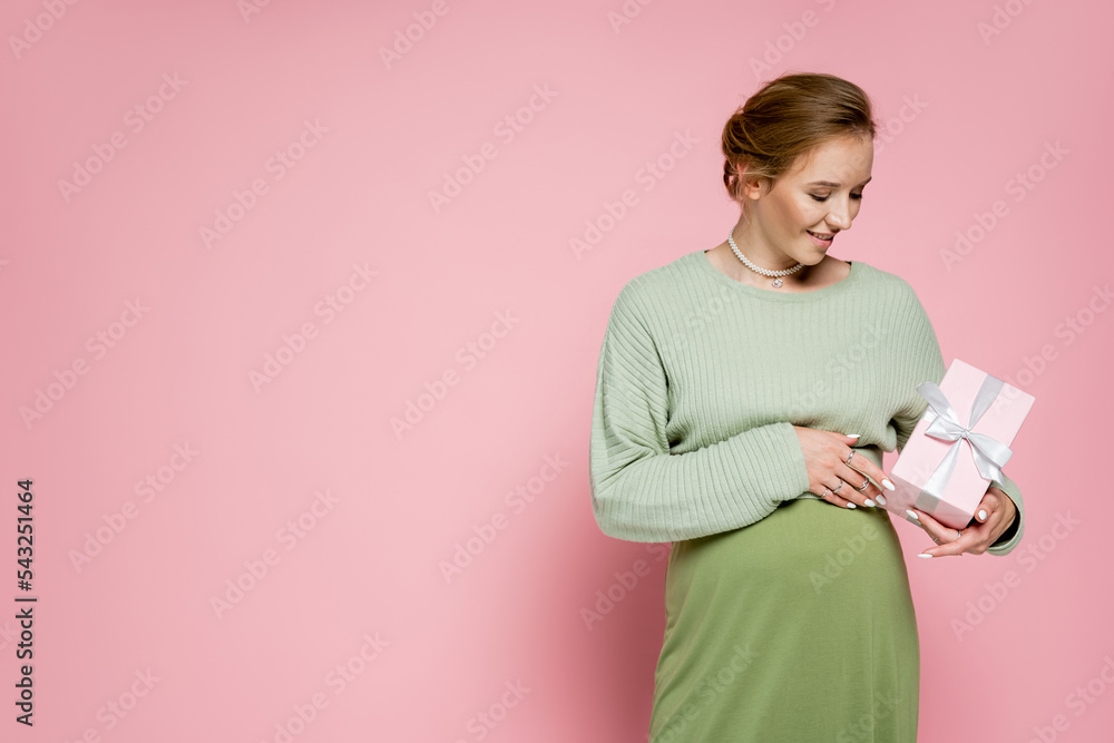 Happy pregnant woman in green outfit holding present on pink background. Happy pregnant woman in green outfit holding present on pink background.