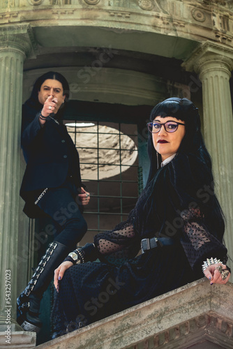 Dark gothic couple in large ancient abandoned mausoleum in neoclassical style with columns and stairs in the forest