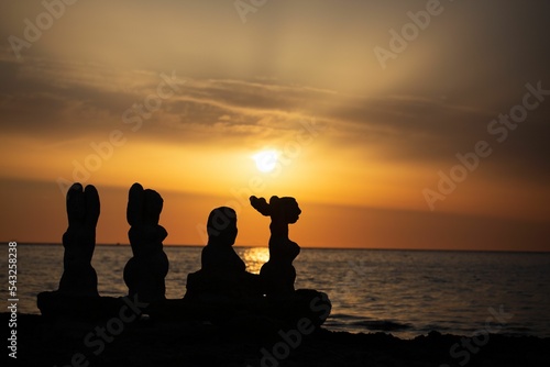 Silhouettes of stone statues on the beach at sunset