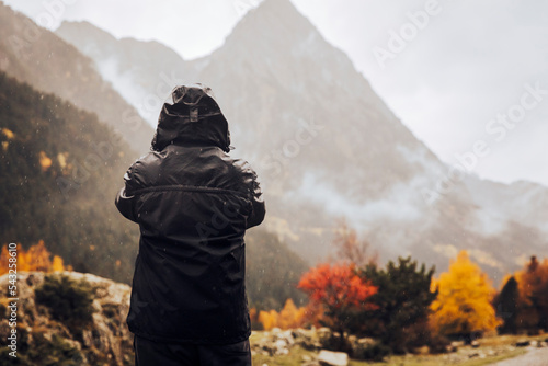 Boy in a raincoat taking photos of an autumn mountain landscape photo