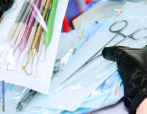A health care worker wearing black gloves holds an instrument packed in sterile bags. A variety of dental instruments packed in sterilization bags.