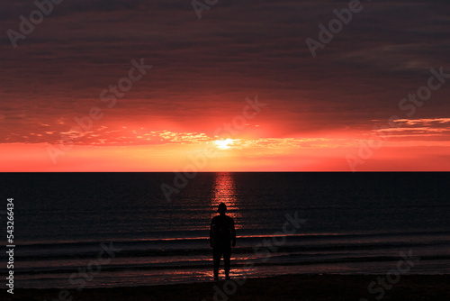 The shore of the Caspian Sea at sunset, pink-orange clouds, water, beach, summer, a person stands on the shore. Silhouette of a man.