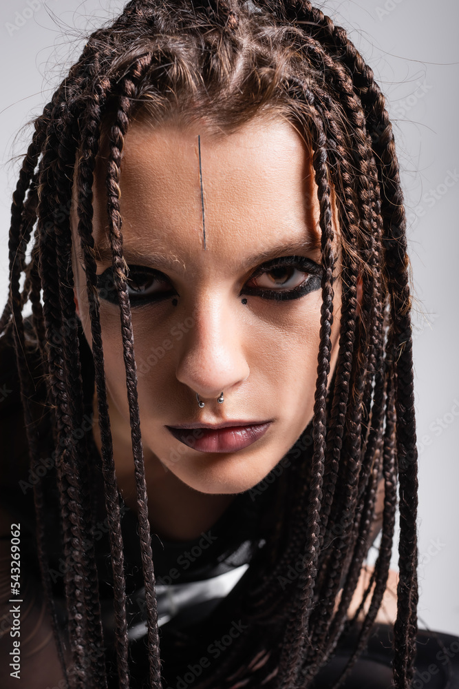 portrait of young woman with futuristic makeup and dreadlocks looking at camera isolated on grey.