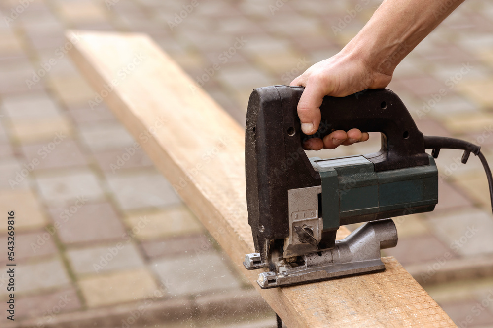 Electric Jigsaw cutting Board or Beam. Male hands of Wood Worker sawing and cutting parts with Electric Hand Jigsaw Close-up Electric Jigsaw cutting Board or Beam. Male hands of Wood Worker sawing and cutting parts with Electric Hand Jigsaw Close-up
