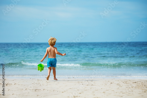 View from behind of a boy running with bucket to ocean waves