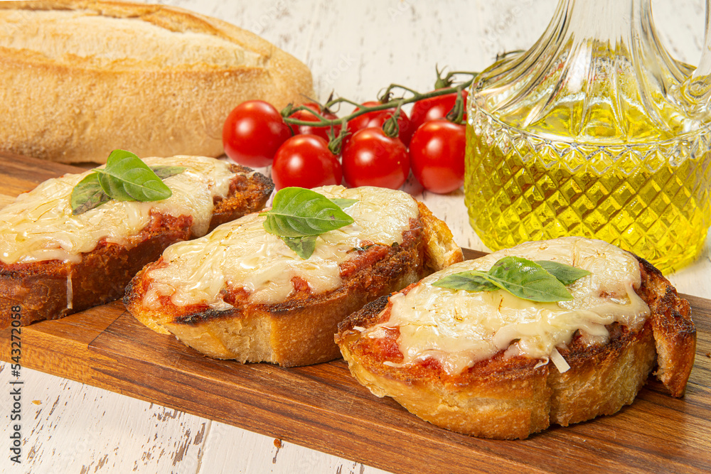 Deliciosas brusquetas com pão italiano, molho de tomate temperado, queijo mussarela e parmesão com folhas de manjericão. Decoração com tomates, pão italiano e azeite de oliva.