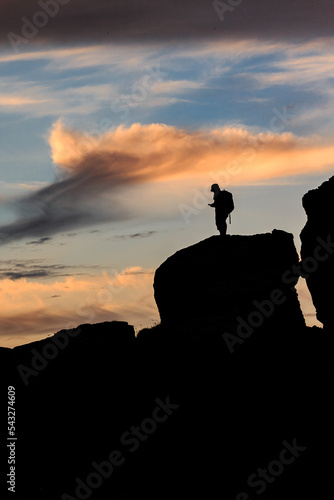 An orange-pink sunset on the black sea against the background of various black mountains  a small silhouette of a person stands on the mountain. Landscape. Vertical orientation.