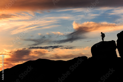 An orange-pink sunset on the black sea against the background of various black mountains, a small silhouette of a person stands on the mountain. Landscape.