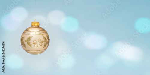 Gold decorated Christmas ball on a light blue background with bokeh effect