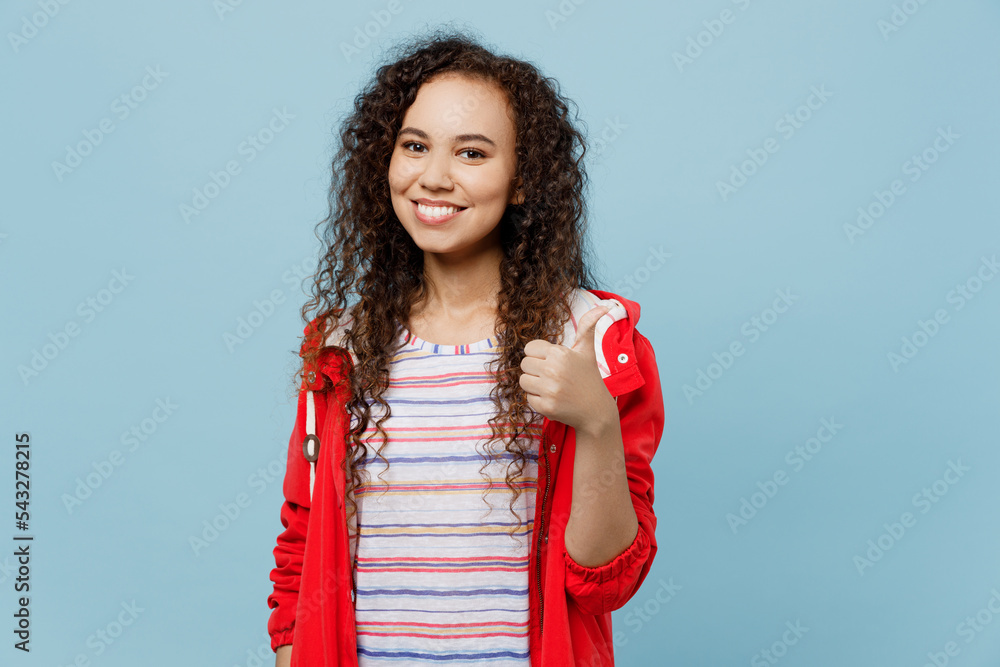 Young smiling happy satisfied woman of African American ethnicity wear red raincoat showing thumb up like gesture isolated on plain pastel light blue cyan background. Wet fall weather season concept. Young smiling happy satisfied woman of African American ethnicity wear red raincoat showing thumb up like gesture isolated on plain pastel light blue cyan background. Wet fall weather season concept.