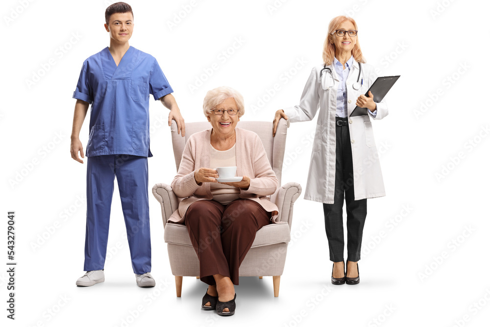 Female doctor and male nurse standing next to an elderly woman in an armchair with a cup of tea Female doctor and male nurse standing next to an elderly woman in an armchair with a cup of tea