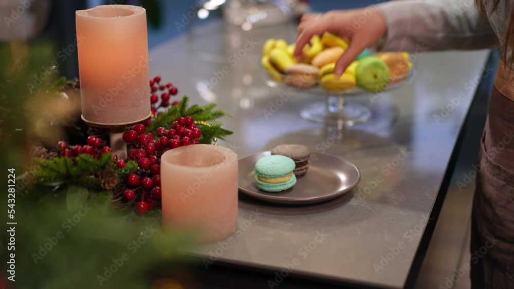 Unrecognizable lady in apron placing multicolored french macaroons on plate on Christmas eve indoors. Young plus-size Caucasian woman preparing delicious traditional snack on New Year at home Unrecognizable lady in apron placing multicolored french macaroons on plate on Christmas eve indoors. Young plus-size Caucasian woman preparing delicious traditional snack on New Year at home