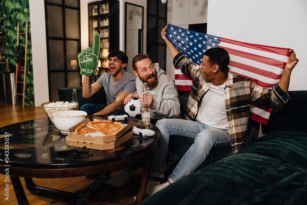 Three excited male fans with american flag and foam glove watching sports match