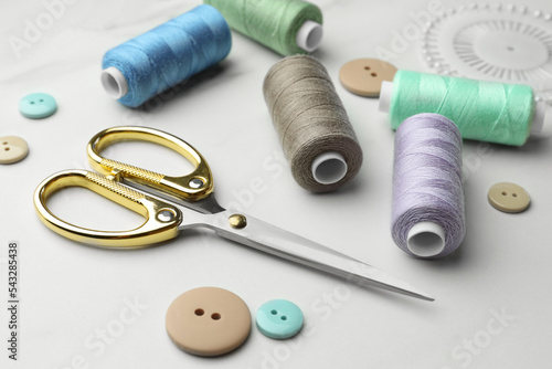 Sewing threads, scissors and buttons on white marble table