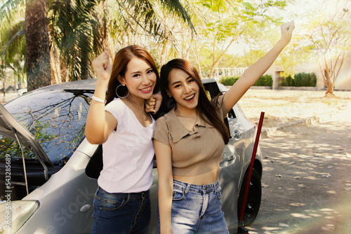 Canvastavla Portrait two carefree asian women parked on the sidewalk enjoying broken car and flat tire as they travel, showing smiles and comfort waiting for help from mechanic