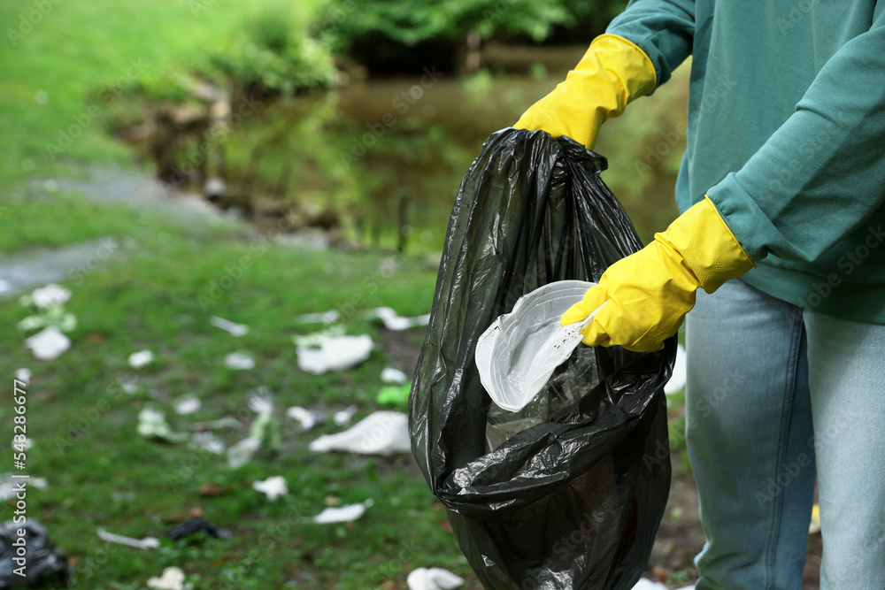 Woman with plastic bag collecting garbage in park, closeup. Space for text