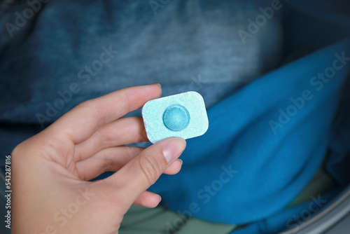 Woman putting water softener tablet into washing machine, closeup