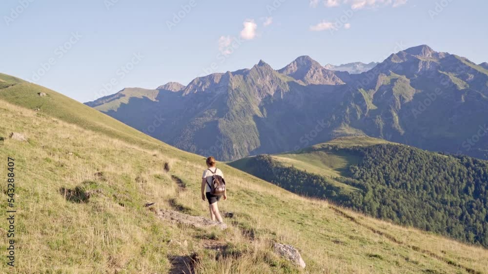 Unrecognizable woman walking on grassy hill slope against rocky mountains Unrecognizable woman walking on grassy hill slope against rocky mountains