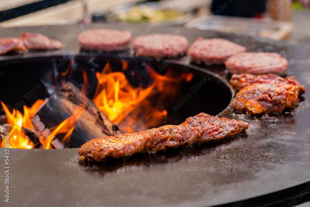 Process of grilling fresh juicy meat steaks and cutlets for burgers on brazier with hot flame at summer local food market: close up. Outdoor cooking, gastronomy, cookery and street food concept Process of grilling fresh juicy meat steaks and cutlets for burgers on brazier with hot flame at summer local food market: close up. Outdoor cooking, gastronomy, cookery and street food concept