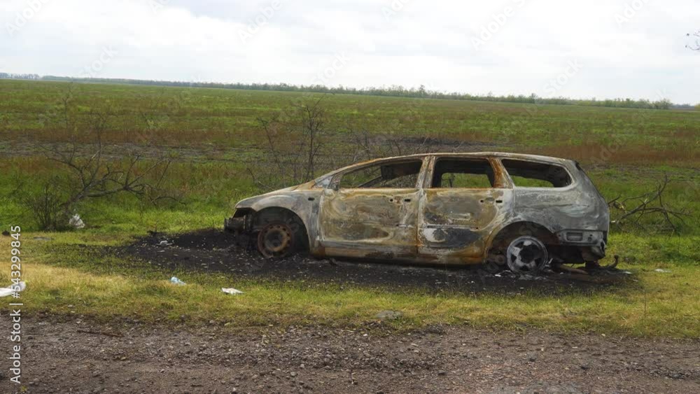 War in Ukraine. 2022 Russian invasion of Ukraine. Countryside. On the side of the road is a destroyed, burned-out civilian car. War crimes. Panorama. The camera moves from left to right War in Ukraine. 2022 Russian invasion of Ukraine. Countryside. On the side of the road is a destroyed, burned-out civilian car. War crimes. Panorama. The camera moves from left to right