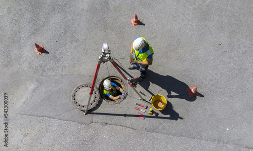 Maintenance and washing of a cesspool through the access of a road manhole. Skilled workers at work lower themselves underground using a pulley photo