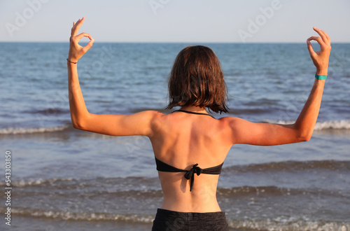 girl from back with developed musculature makes OM YOGA sign by the sea photo
