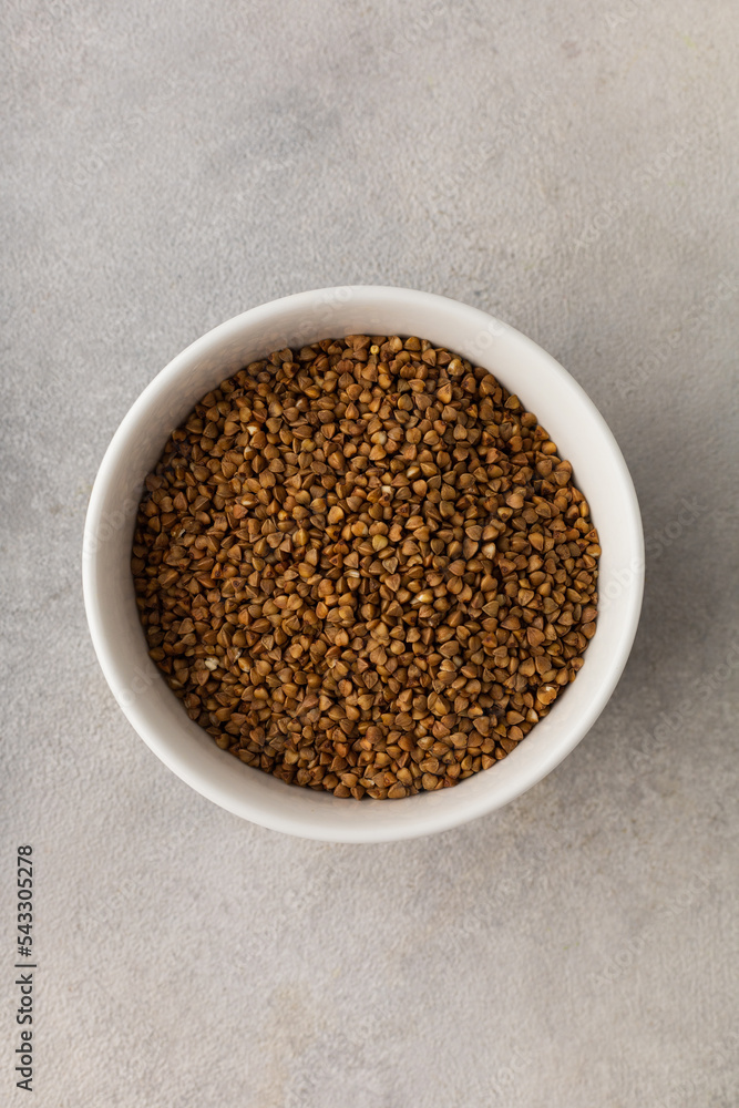 A bowl of dry buckwheat before cooking on a light gray background A bowl of dry buckwheat before cooking on a light gray background