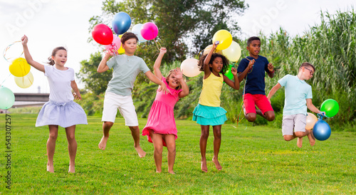 Barefoot children jumping on field with balloons in hands and smiling.