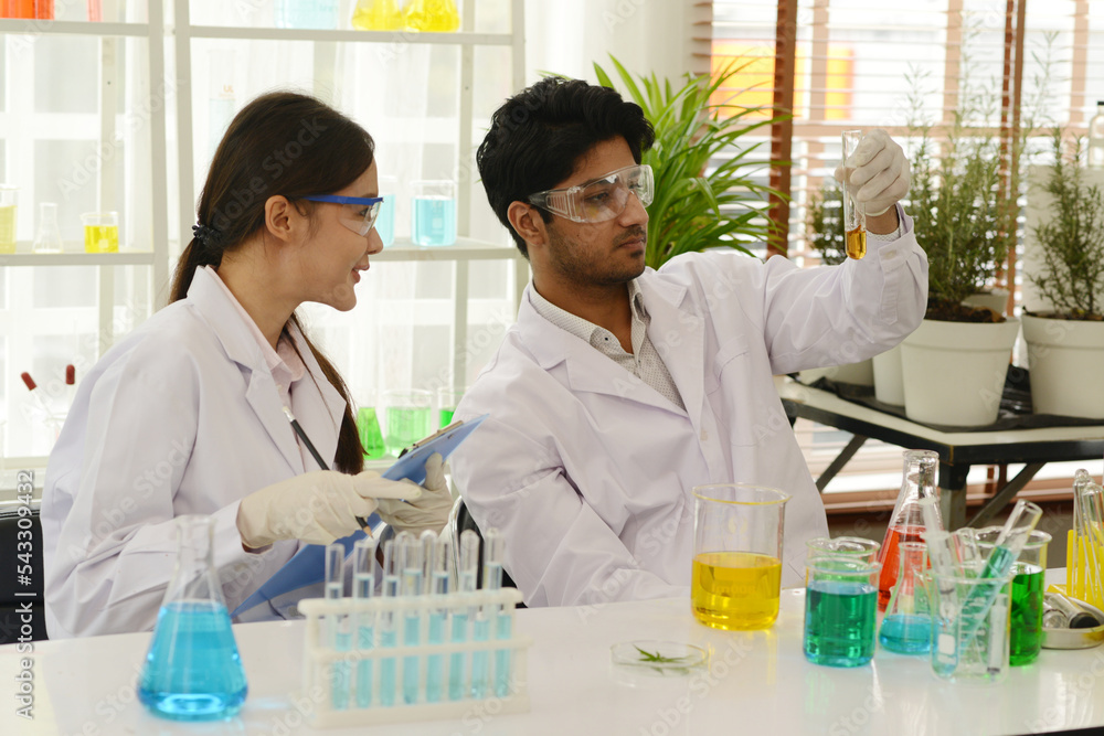 Portrait of a scientist working in a laboratory examining test tubes with colorful liquids. and a female chemist is recording the day. Portrait of a scientist working in a laboratory examining test tubes with colorful liquids. and a female chemist is recording the day.