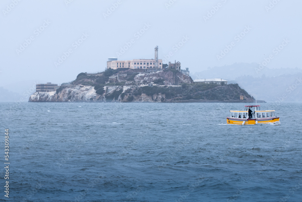 Alcatraz Island with a yellow tourist ferry in the San Fransisco Bay on a foggy day
