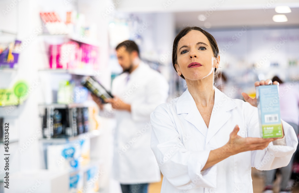 Confident young adult woman pharmacist offering product, working at pharmacy