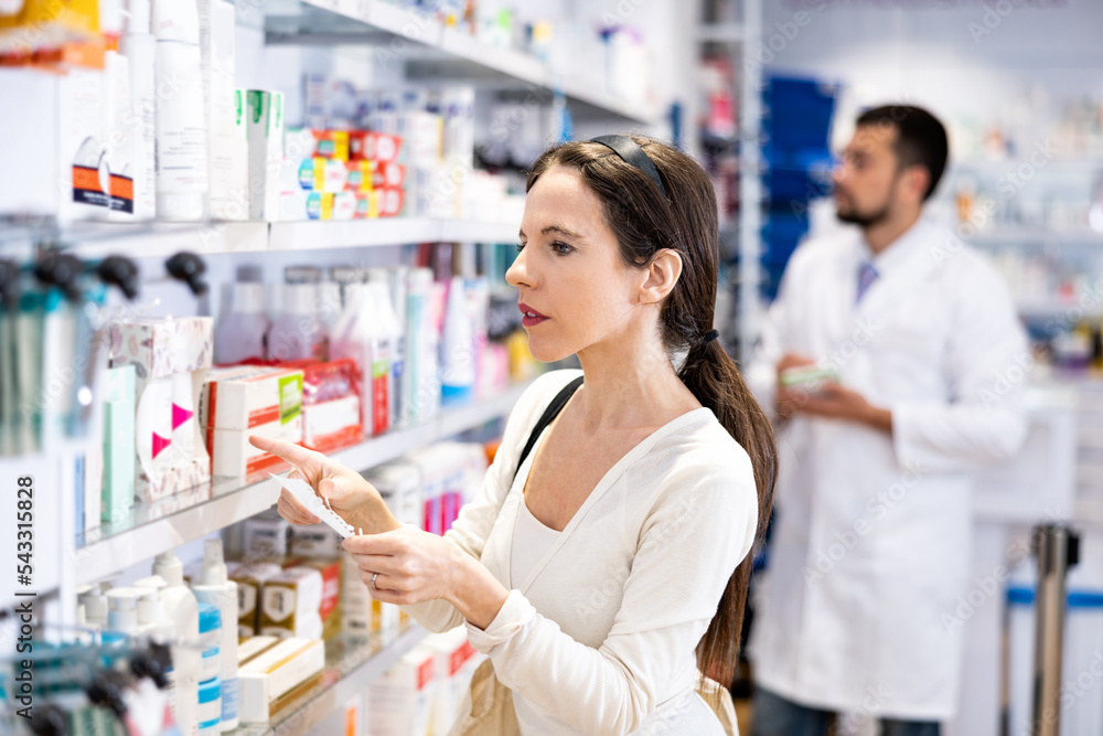 Focused young woman choosing products with shopping list at drug store