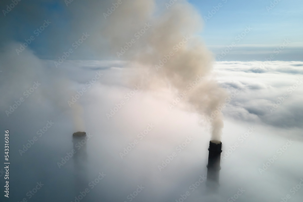 Coal power plant high pipes emitting black poisonous smoke moving upwards over white fog polluting air. Production of electrical energy with fossil fuel concept